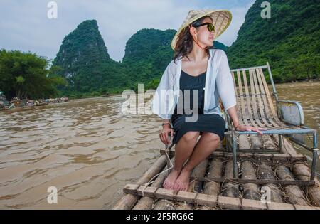 woman in traditional Asian sitting on bamboo raft in Yangshuo Stock Photo