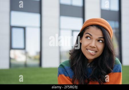 Beautiful African American woman biting her lip, thinking, looking to copy space, standing outdoors