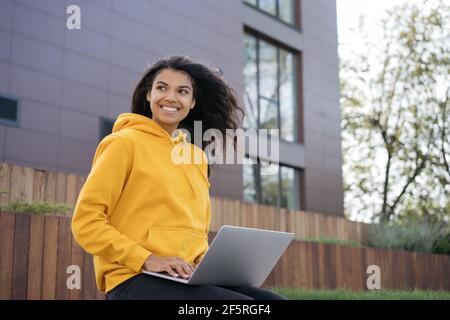 Beautiful smiling African American woman using laptop computer, working freelance project. Portrait of young confident designer sitting at workplace