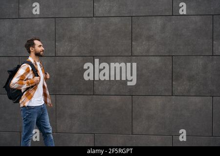 Young bearded man with backpack walking on street, isolated on background. Travel concept Stock Photo
