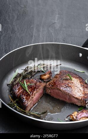 Medium  grilled beef steak in frying pan on black stone background Stock Photo