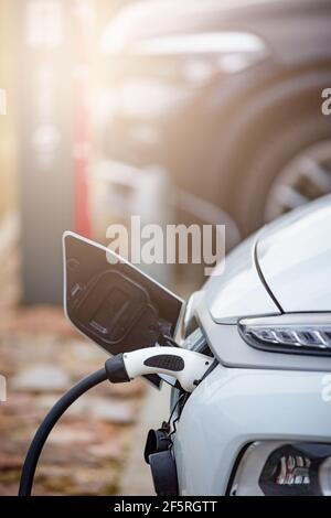 Selective focus shot of an electric car at a charging station with the power cable plugged in Stock Photo