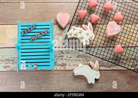 Rabbit-shaped cookies surrounded by heart-shaped cookies, white chocolate with pink edible paint and a blue wooden basket written in Portuguese: Happy Stock Photo