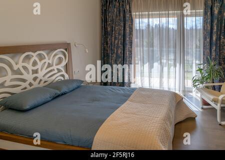 Cozy bright spacious bedroom interior in private house on a sunny spring day. Original retro style double bed with pillows and  cover near the window Stock Photo