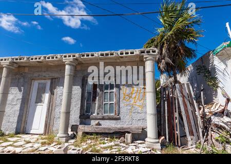 Rundown house in a coastal village that appears to be abandoned. Close to the beach. Blue sky and palm tree on a sunny day. Stock Photo