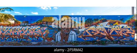 Street art in a small town Mexico on a long wall featuring an old man wearing a straw hat, a rustic hut and words, with a blue sky above the wall Stock Photo