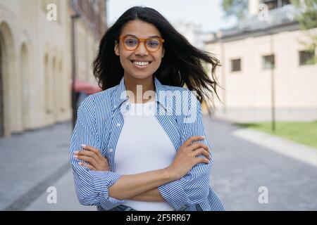 Portrait of beautiful smiling African American woman looking at camera, standing on the street. Young confident businesswoman posing for pictures Stock Photo
