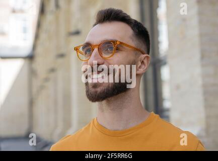 Close up portrait of handsome smiling bearded man wearing stylish eyeglasses looking away on the street Stock Photo