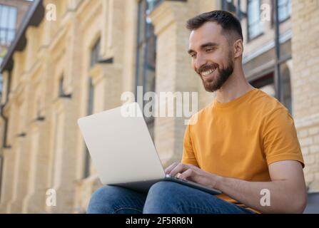 Young handsome programmer using laptop computer. Smiling man copywriter typing, communication, working online Stock Photo