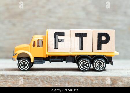 Toy truck hold alphabet letter block in word FTP (Abbreviation of File Transfer Protocol) on wood background Stock Photo