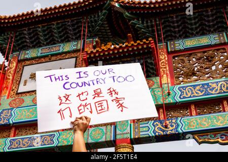 Washington, DC, USA, 27 March, 2021.  Pictured: A protester raises a sign overhead, reminding Americans that 'this is our country too,' at the Chinatown Gate in downtown DC.  Credit: Allison C Bailey/Alamy Live News