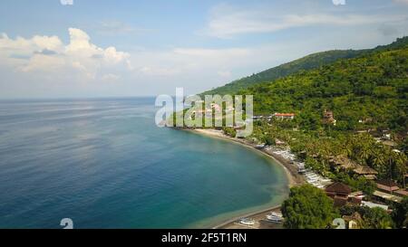 Aerial photo of a wild beach in Bali. A long strip of beach and a steep mountain slope covered with greenery. Wild beach in Bali with yellow sand and Stock Photo