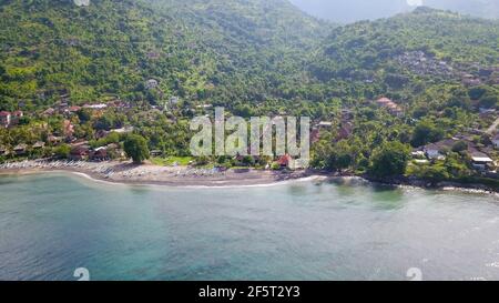 Aerial photo of a wild beach in Bali. A long strip of beach and a steep mountain slope covered with greenery. Wild beach in Bali with yellow sand and Stock Photo