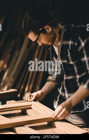 Carpenter man attend to making masterpiece woodworks handcrafted furniture fine measure in wood workshop, Vertical shot. Stock Photo