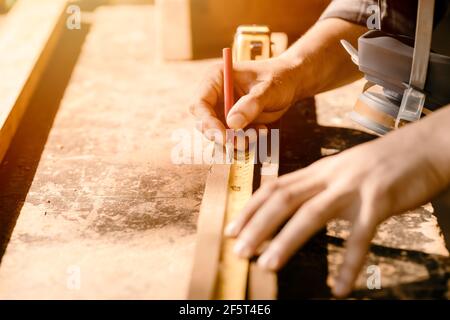 Carpenter man working in furniture wood workshop, Closeup hand measuring and mark on wooden piece. Stock Photo