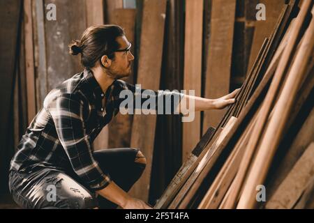 Carpenter man working in furniture wood workshop, selecting wooden board. Stock Photo