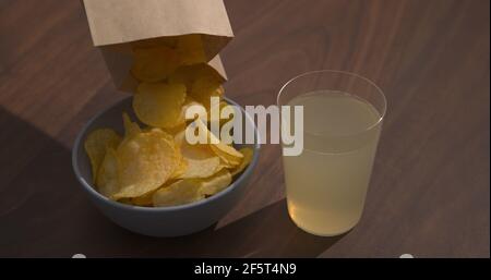Man hand pour potato chips to blue bowl with ginger beer on background, wide photo Stock Photo