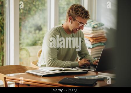 Smiling man working on laptop. Man staying at home using laptop and smiling. Stock Photo