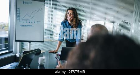 Smiling businesswoman standing at table and discussing finance with team. businesswoman giving presentation over a project budget to colleagues in off Stock Photo