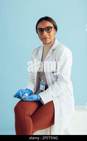 Portrait of a confident doctor on blue background. General practitioner wearing lab coat and hand gloves looking at camera. Stock Photo
