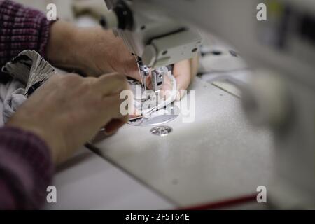 Shallow depth of field (selective focus) image with the hands of a senior woman working at an electric sewing machine in a textile factory. Stock Photo