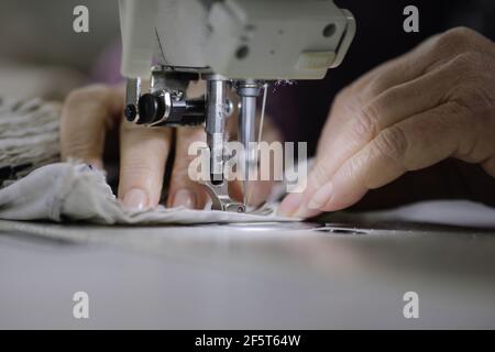 Shallow depth of field (selective focus) image with the hands of a senior woman working at an electric sewing machine in a textile factory. Stock Photo