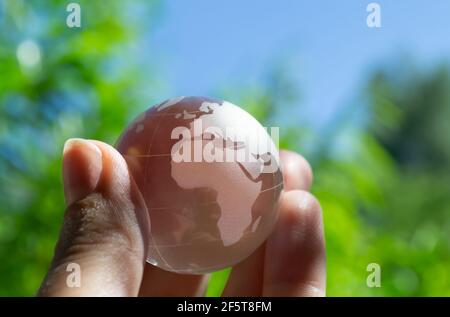 Crystal globe in the hand of a man against a background of blue sky and green foliage. Earth protection concept. Earth Day Stock Photo