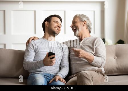 Smiling older father and adult son laugh using smartphone Stock Photo
