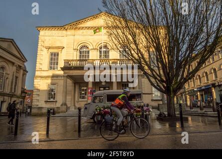 Stroud Subscription Rooms. Ranked by the Sunday Times as the best place to live in the UK 2021. Iconic building in the town centre. Peoples Republic of Stroud flag flying on Cotswold stone building. Cyclist riding through the square. Stock Photo