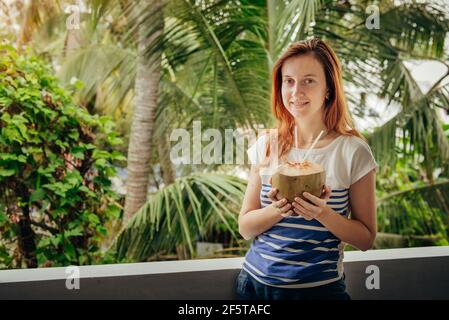 Young caucasian woman drinking fresh coconuts and enjoying a tropical vacation in Kerala, south India Stock Photo