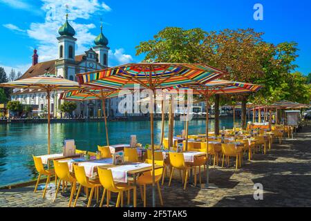 Cozy waterfront street restaurant on the shore of the Reuss river. Street cafe with colorful umbrellas on the walkway, Lucerne, Switzerland, Europe Stock Photo