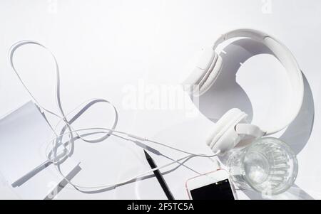 On a white background, white headphones, a telephone, white sheets for writing and a black pencil. A glass of water. Border for business and leisure. Stock Photo