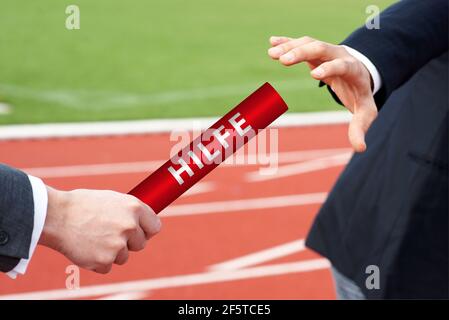 Businessmen pass help baton in German Hilfe relay race in stadium Stock Photo