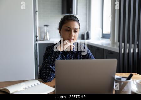 Close up thoughtful Indian woman looking at laptop screen Stock Photo
