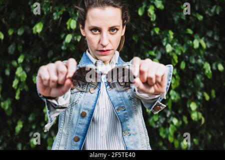 Determined female in denim jacket standing with trendy round sunglasses in park and looking at camera Stock Photo