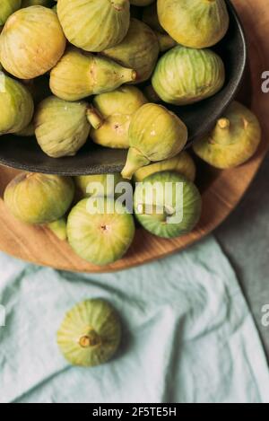 Fresh and ripe sweet green figs, in a black bowl on the wood plate served on the blue tablecloth table, Seasonal organic fruit. Also known as ripe whi Stock Photo