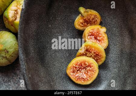 Green fig slices in modern black bowl on the table with grunge texture. minimal concept food. Also known as ripe white figs Stock Photo