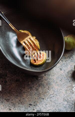 Green fig slices in modern black bowl on the table with grunge texture. minimal concept food. Also known as ripe white figs Stock Photo