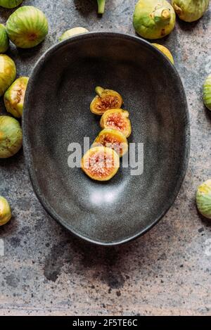 Green fig slices in modern black bowl on the table with grunge texture. minimal concept food. Also known as ripe white figs Stock Photo