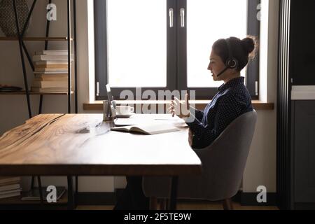 Side view serious Indian woman wearing headset using laptop Stock Photo