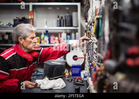 Side view of aged skilled repairman taking professional tools from rack while working in service workshop Stock Photo