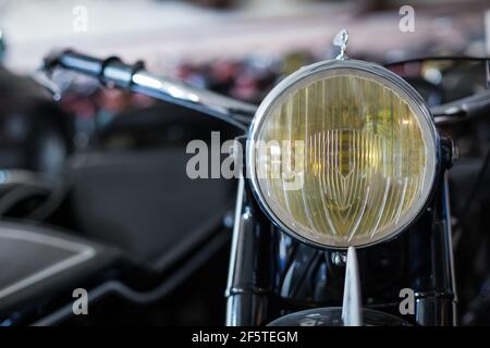 Closeup of yellow headlight of old fashioned motorbike placed against blurred background of workshop Stock Photo