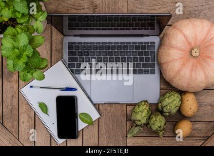 From above of various vegetables arranged on wooden table with gadgets and notepad with pen Stock Photo
