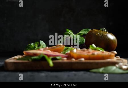 Fresh ripe sliced black tomatoes and green mint stems on wooden cutting board on black background Stock Photo