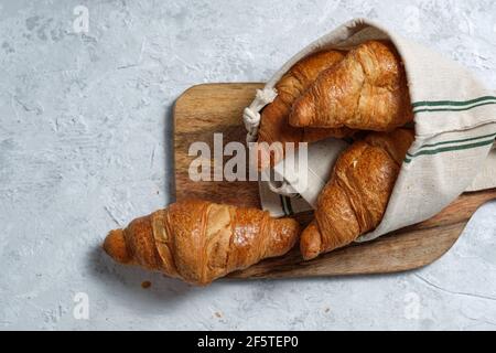 Freshly baked croissants served on wooden cutting board with napkin on table for breakfast Stock Photo
