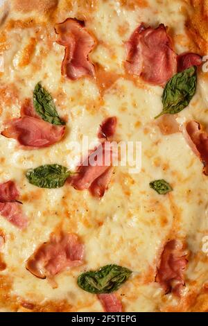 Close-up of tasty homemade pizza with basil and ham served on on table Stock Photo