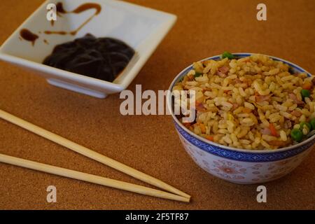 Special Fried rice in a bowl, soy sauce and Asian Chopsticks in a wooden table Stock Photo