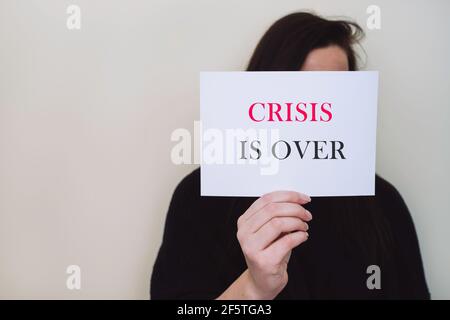 Woman holding white card with text CRISIS IS OVER isolated on beige background. Hand holding a sign with words crisis is over. Stock Photo