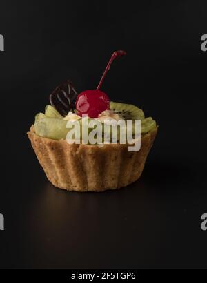 Fruit dessert cake with cherries, shecolade leaf, kiwi wedges and protein cream, on a black background isolated Stock Photo