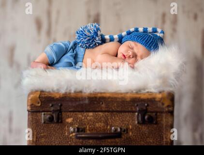 little newborn baby is sleeping on a white fur blanket on top of old  suitcases Stock Photo